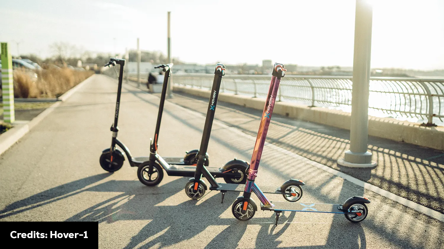 Three scooters are lined up on a sidewalk next to a body of water, offering a picturesque scene for scooter enthusiasts or anyone seeking outdoor leisure. Scooter Advice