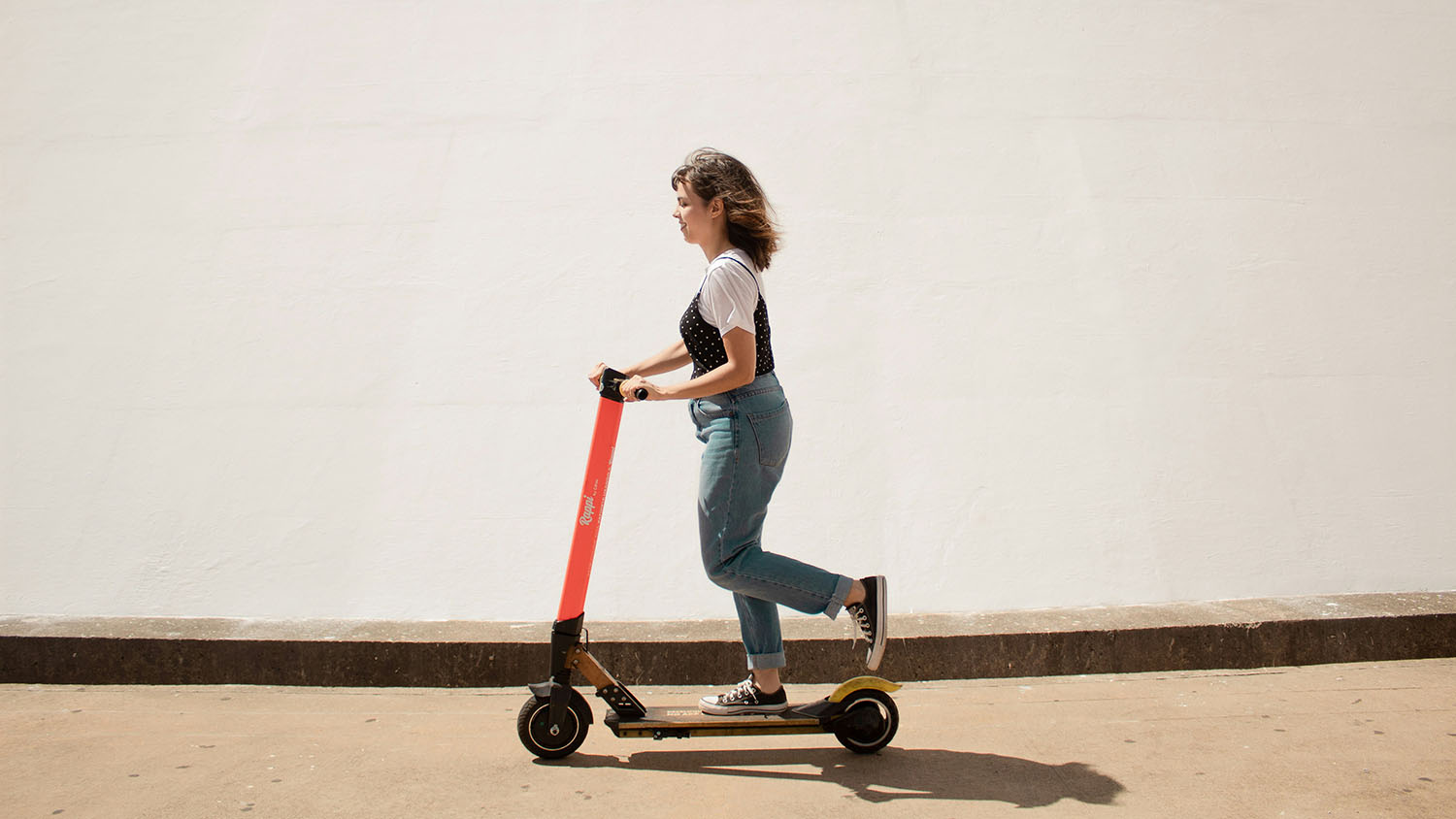 A woman riding an electric scooter in front of a white wall. Scooter Advice