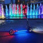 A scooter with colorful lights parked beside a mesmerizing fountain. Scooter Advice