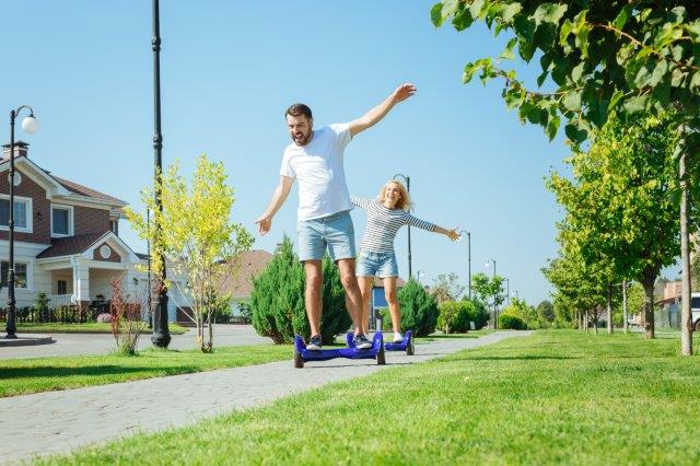 Man and girl balancing on a hoverboard outdoors on a sunny day. Scooter Advice 360