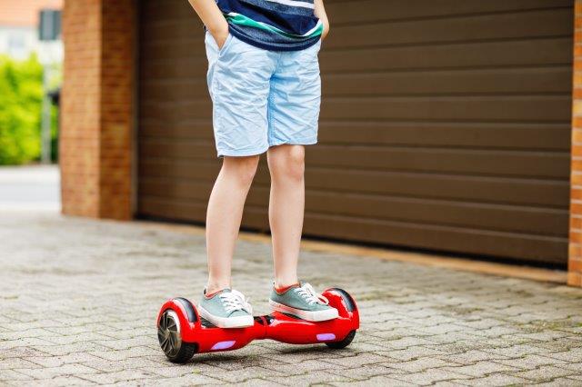 Child riding a red hoverboard on a paved driveway. Scooter Advice 360