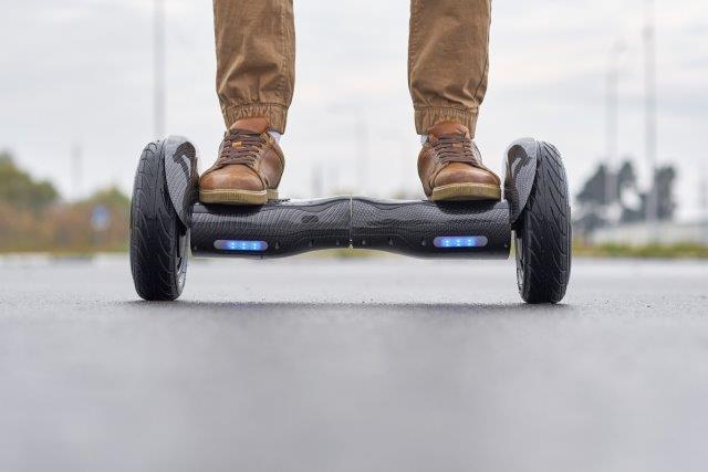 Person standing on a hoverboard on an asphalt surface. Scooter Advice 360
