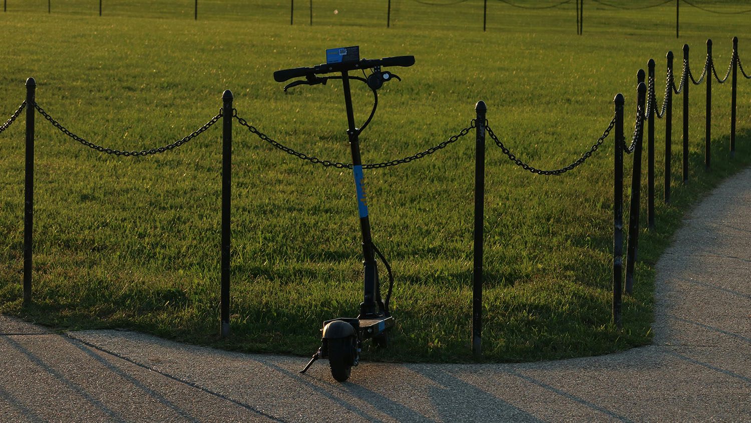 A scooter is parked in a grassy area next to a fence. There is no connection to the provided keyword "how much is a segway" within the modified description. Scooter Advice