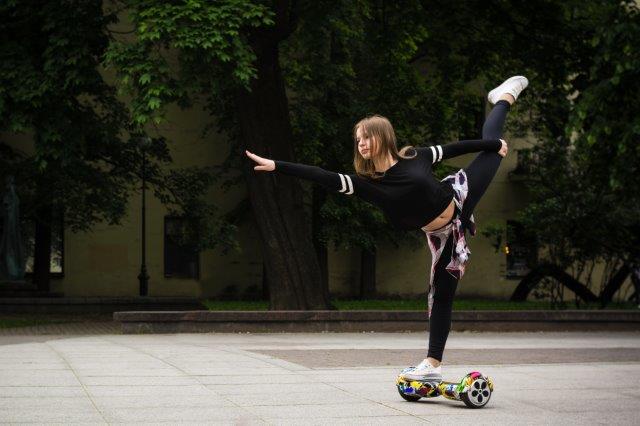 Woman performing a one-legged balance on a hoverboard outdoors. Scooter Advice 360