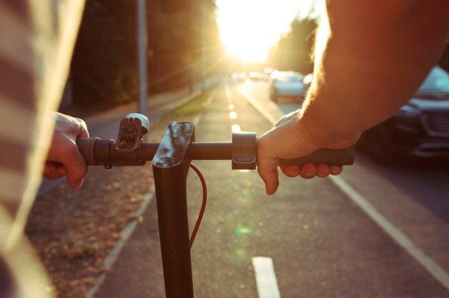 A person riding a scooter on a street at sunset. Scooter Advice 360