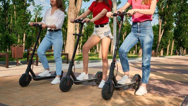 Three women riding electric scooters in a park. Scooter Advice 360