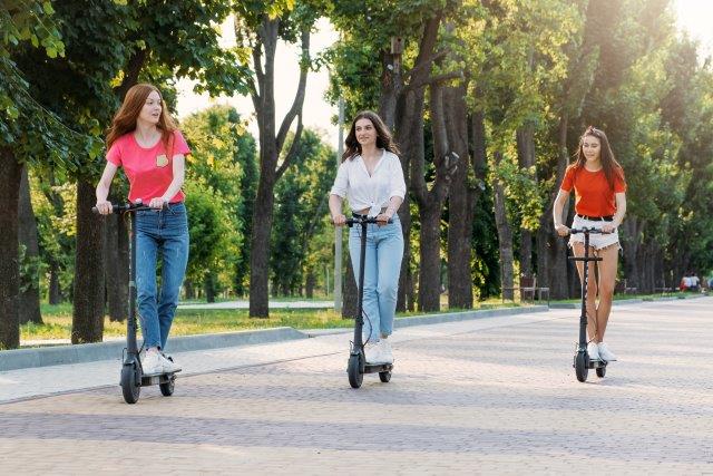 Three young women riding electric scooters in the park. Scooter Advice 360