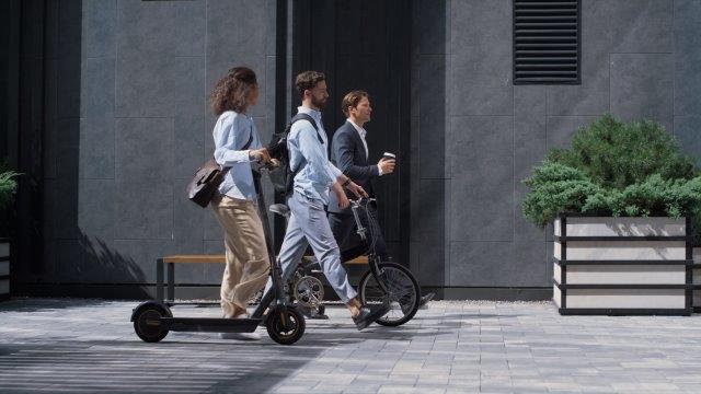 A group of people riding electric scooters in front of a building. Cheap Electric Scooters for Adults With Seat. Scooter Advice 360