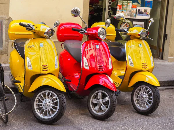 Three colorful Vespa scooters parked side by side, with the central one being red and the outer ones yellow. Scooter Advice 360