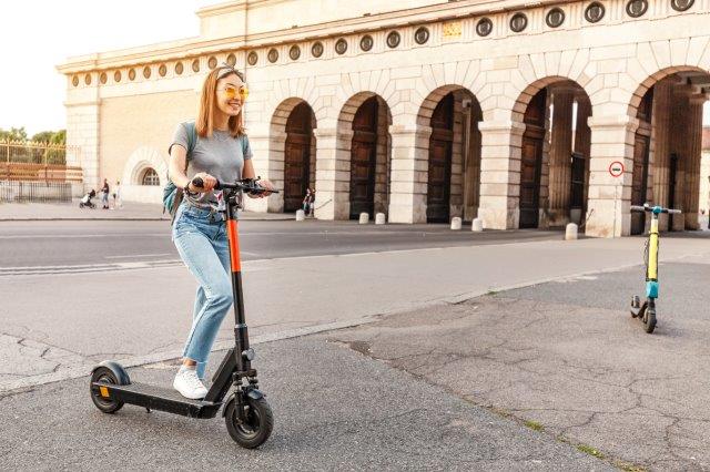 A woman riding an electric scooter in front of a building. Scooter Advice 360