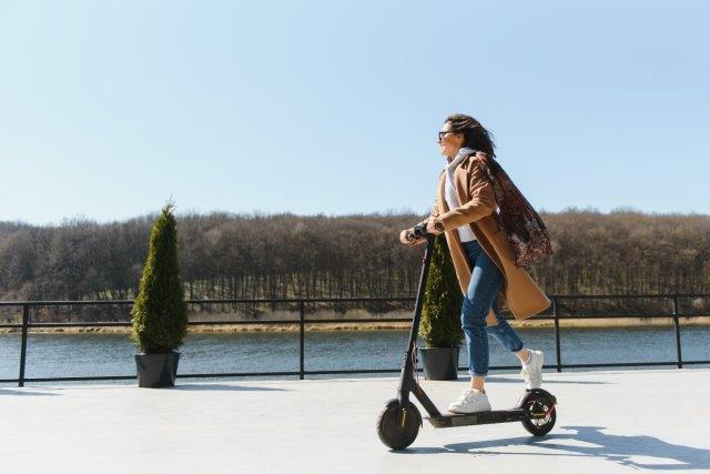 A woman riding an electric scooter near a lake. Best Electric Scooter Under 1000. Scooter Advice 360