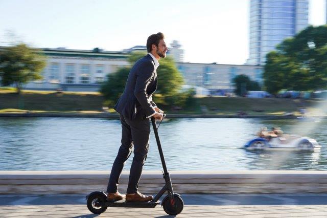 A man in a suit riding an electric scooter. How to Ride Electric Scooter. Scooter Advice 360