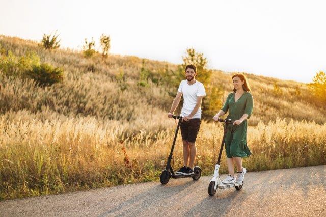 Two people riding electric scooters on a road in the countryside. Scooter Advice 360