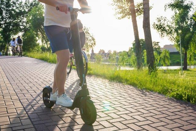 A man riding an electric scooter in a park. Sit Down Electric Scooter for Adults. Scooter Advice 360