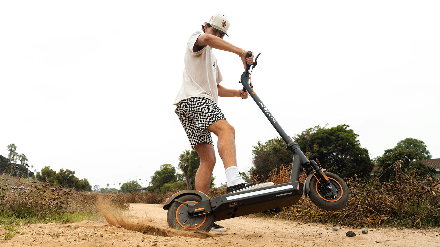 A man riding an electric scooter down a dirt road, wondering if it can be taken on a plane. Scooter Advice