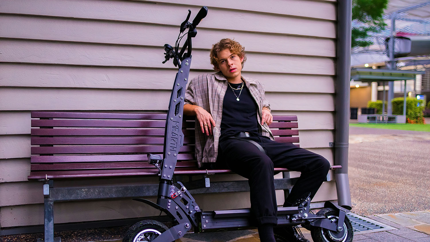 A man sitting on a bench next to an electric scooter, pondering whether he can take it on a plane. Scooter Advice