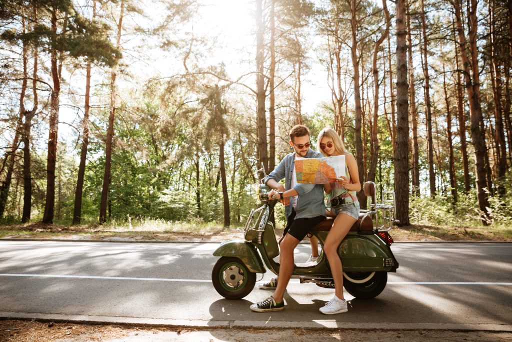 Two people examining a map together while seated on a scooter by the roadside in a wooded area. Scooter Advice 360