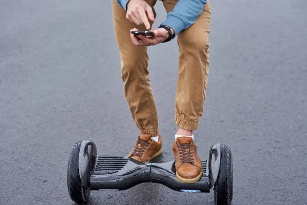 Person using a smartphone while standing on a hoverboard. Scooter Advice 360