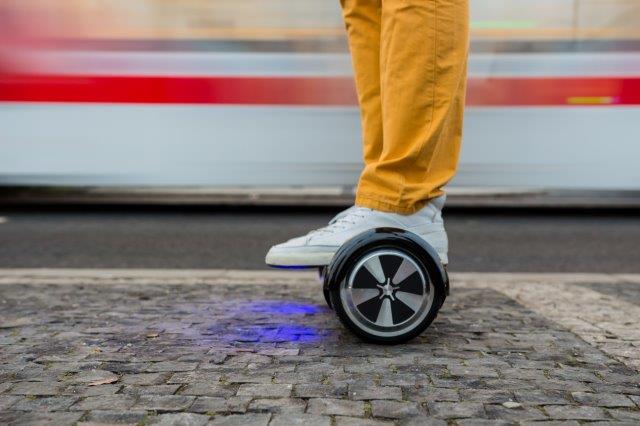 Person riding a hoverboard on a city sidewalk with a blurry background indicating motion. Scooter Advice 360