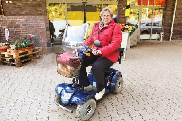 A woman on a blue mobility scooter in front of a store. Scooter Advice