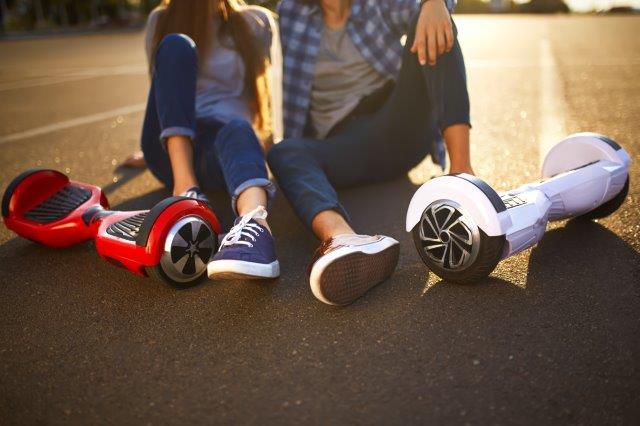 Two people sitting on the ground next to their hoverboards, enjoying a sunny day outside. Scooter Advice 360
