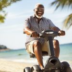 A joyful senior man riding a mobility scooter on a beachside promenade. Scooter Advice 360
