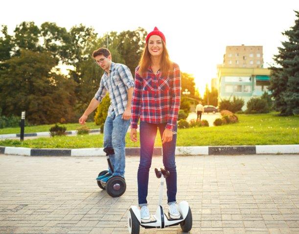 Two people enjoying a sunny day outdoors with one riding a hoverboard and the other on a unicycle. Scooter Advice 360