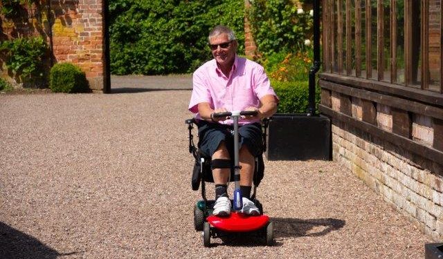 A man in a pink shirt riding a red mobility scooter. Scooter Advice