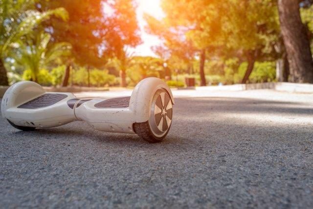 A used white hoverboard on a sunlit concrete path with trees in the background. Scooter Advice 360