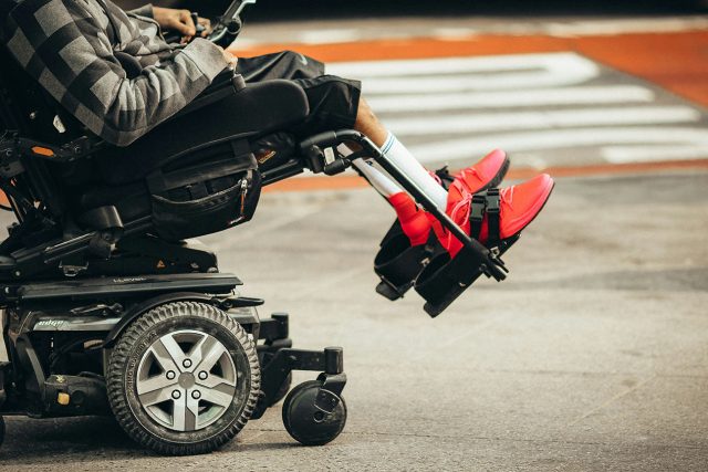 A elderly man utilizing a mobility aid, sitting in a wheelchair on a street. Scooter Advice