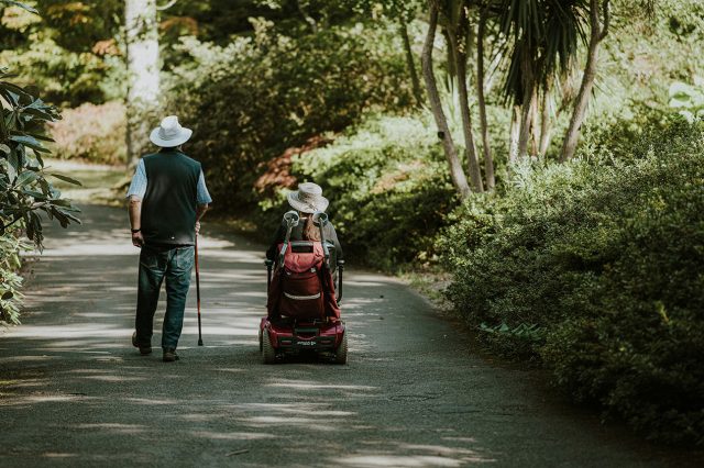 A man and a woman walking down a path, discussing whether Medicaid will cover the cost of a power chair. Scooter Advice