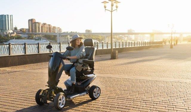 A woman is riding a scooter on a sidewalk. Where Is The Speed Limiter On A Pride Mobility Scooter? Scooter Advice
