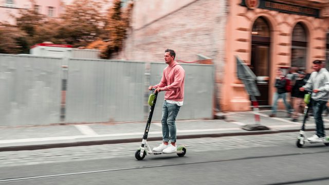 Two men riding scooters down a street, questioning if electric scooters are legal in NYC. Scooter Advice