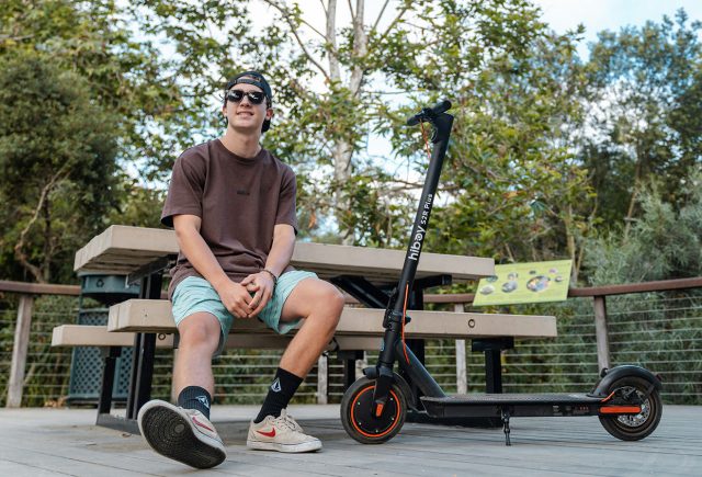 A man sitting on a bench next to a scooter, wondering how long does an electric scooter charge last. Scooter Advice