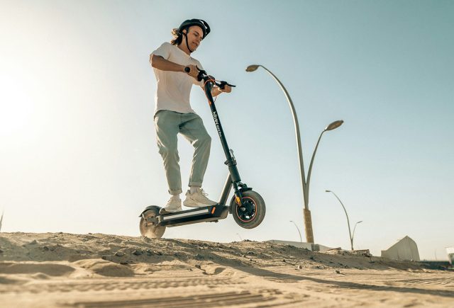 A man enjoying a ride on an electric scooter in the desert, wondering how long the charge will last. Scooter Advice