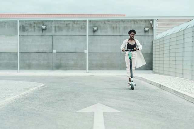 A woman is riding an electric scooter in a parking lot. Scooter Advice