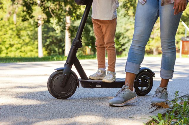 A woman and child standing next to an electric scooter, demonstrating how to charge it without a charger. Scooter Advice