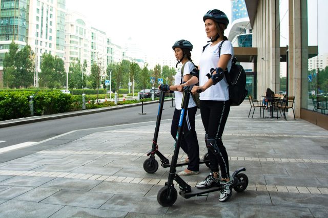 Two people riding electric scooters in a city. Scooter Advice