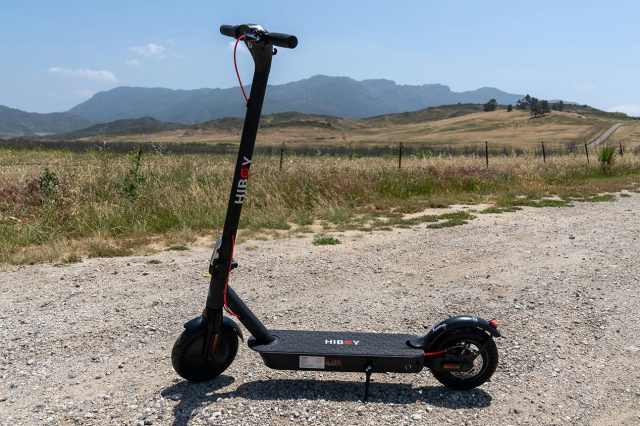 An electric scooter sitting on a dirt road with mountains in the background. Scooter Advice