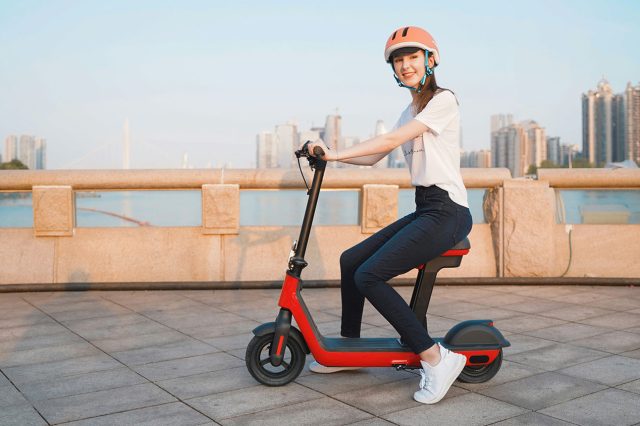 A woman riding an electric scooter in front of a city tries to figure out why won't my electric scooter turn on. Scooter Advice