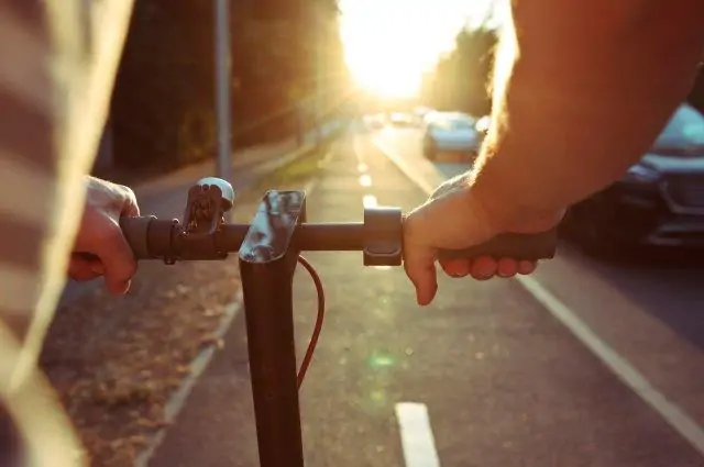 A person riding a scooter on a street at sunset. Scooter Advice 360